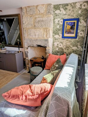 Ett mysigt vardagsrum med en vägg av sten, en soffa med mönstrade kuddar, ett inramat konstverk och en trappa i bakgrunden.