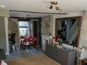En matplats med en vägg av sten, ett matbord med stolar, en öppen spis och en stor spegel.