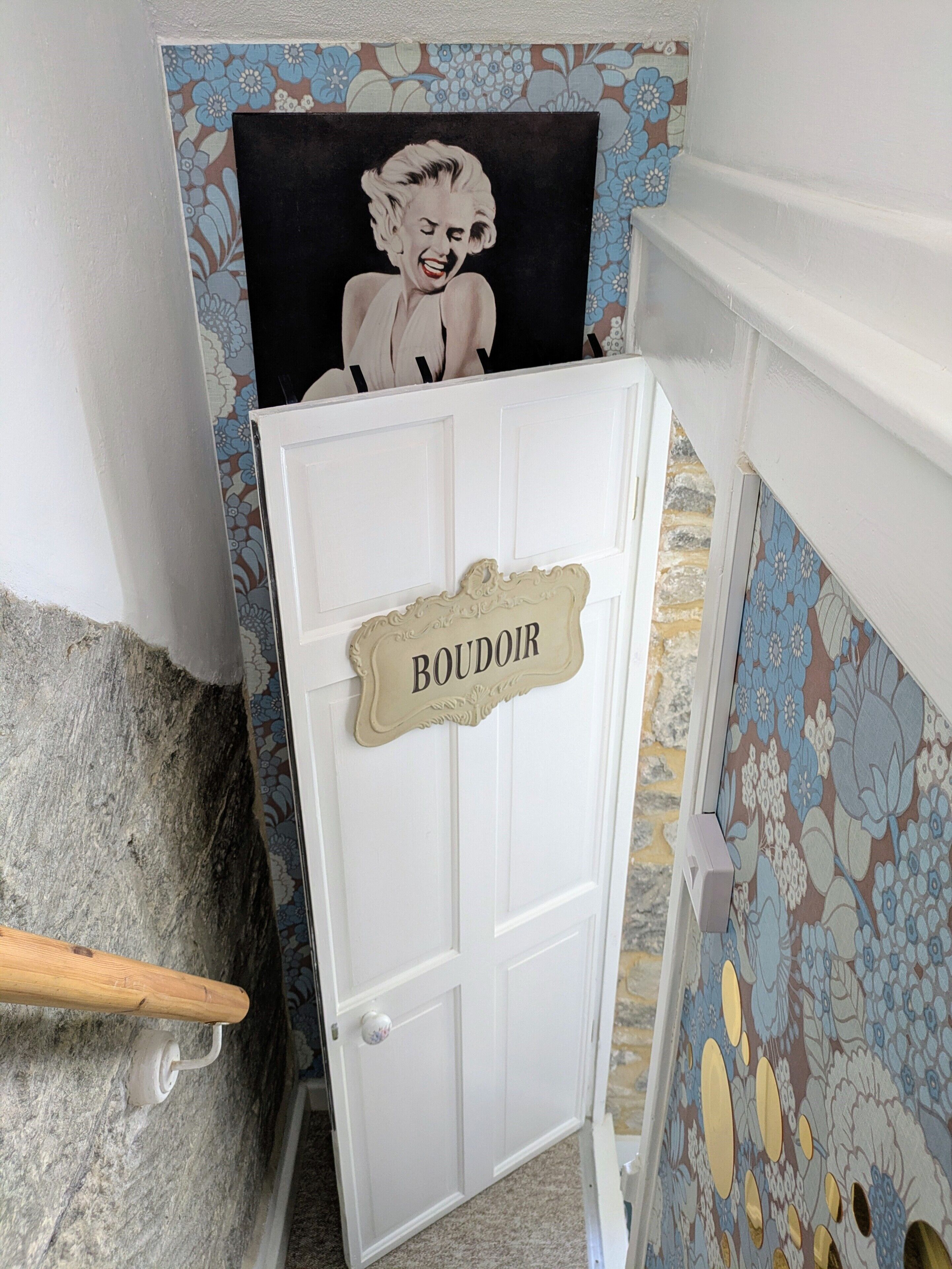 Une porte blanche avec une pancarte indiquant « BOUDOIR », un mur orné de motifs et une vue partielle d’un banc en bois.