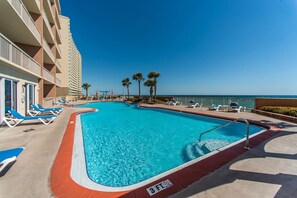 A swimming pool with blue water, surrounded by lounge chairs and palm trees. - Sunrise Beach #1203 (Panama City Beach)