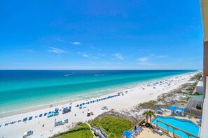 A beach view with a pool area, beach umbrellas, and lounge chairs. - Sunrise Beach #1203 (Panama City Beach)