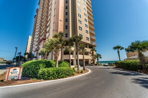 A multi-story hotel with a parking garage sign, surrounded by palm trees and a clear blue sky. - Sunrise Beach #1203 (Panama City Beach)