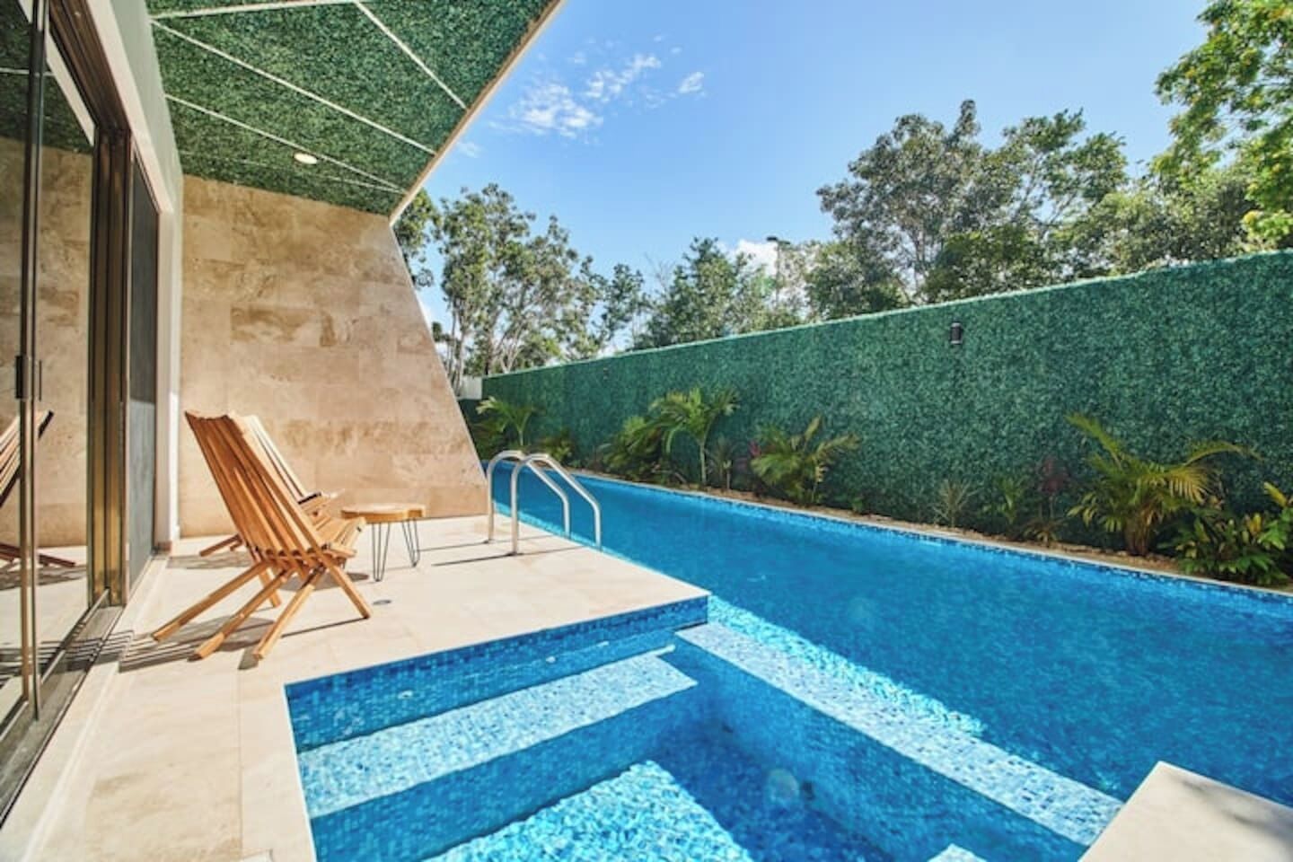 A swimming pool with steps leading into it, surrounded by a green wall and trees.
