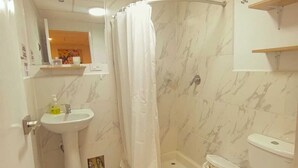 Un baño con lavamanos pedestal, ducha con cortina, inodoro y espejo sobre el lavamanos.