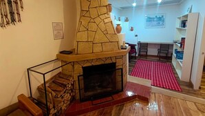 Una sala de estar con chimenea de piedra, una escalera, un tapete rojo a cuadros y una estantería.