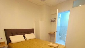 Un dormitorio con cama, suelo de madera, cabecero y puerta que da a un baño.