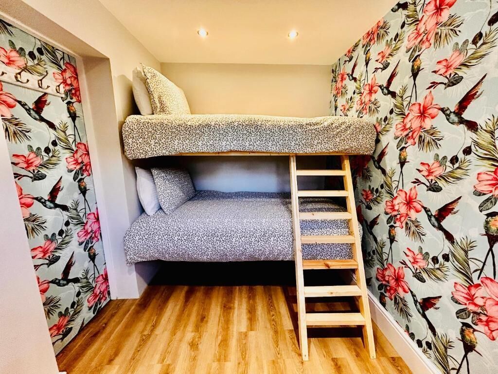 Uma cama beliche com escada, soalho de madeira e papel de parede floral.