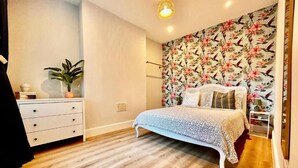 Une chambre à coucher avec un lit, une commode, une plante en pot et un papier peint à motifs floraux.