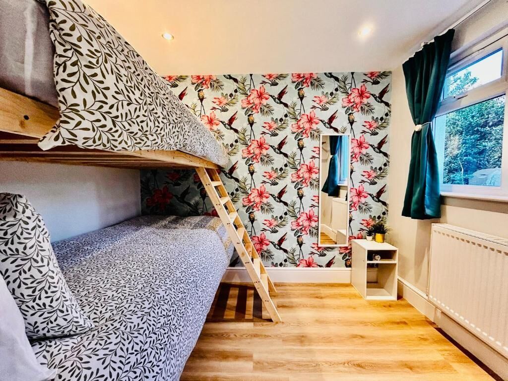 Une chambre avec un lit superposé, un papier peint à motifs floraux, une petite table et une fenêtre avec des rideaux.