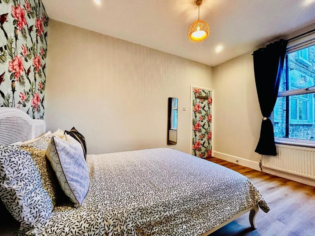 Quarto com cama, radiador, janela com cortinas e luminária fixada na parede.