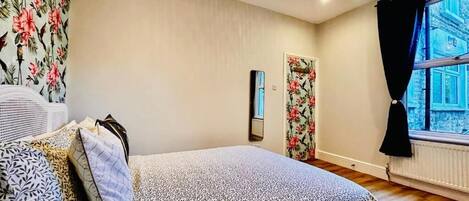 A bedroom with a bed, a radiator, a window with curtains, and a wall-mounted light fixture.