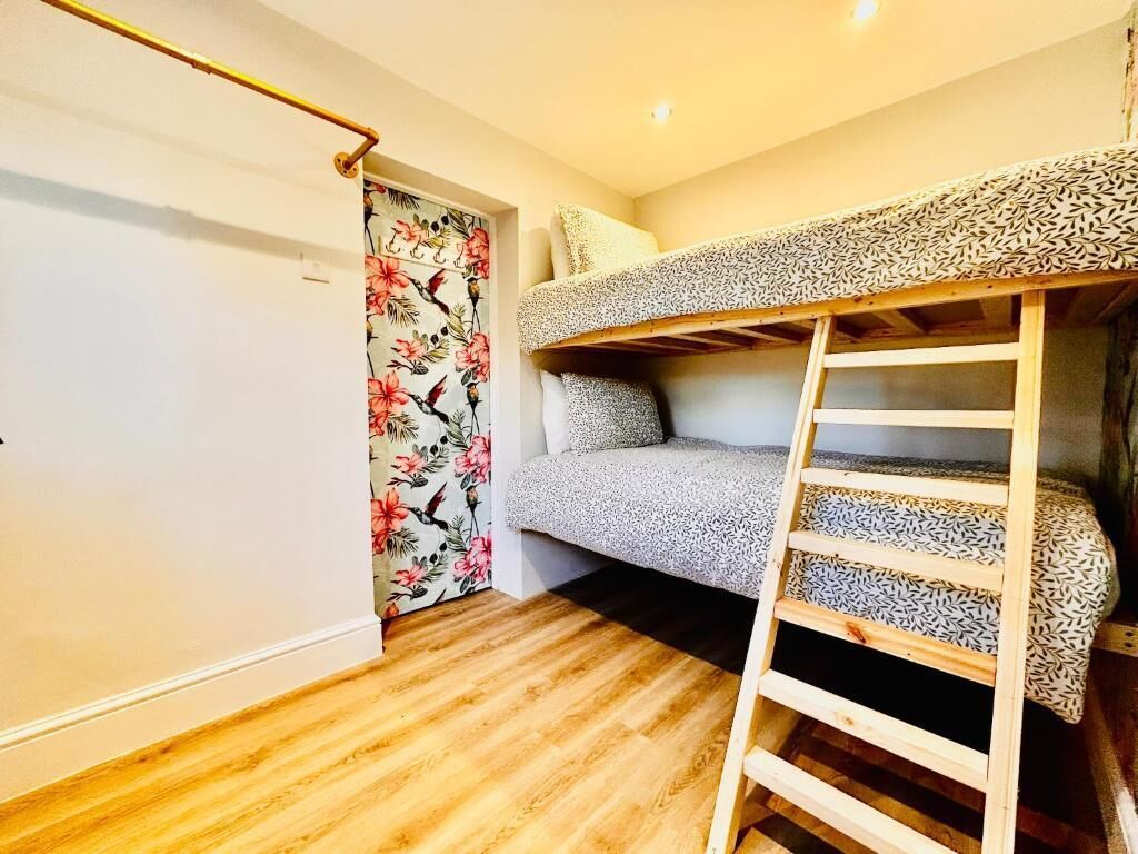 A bunk bed with a ladder, a floral-patterned door, and wooden flooring.