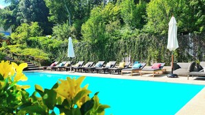A pool area with lounge chairs and umbrellas, surrounded by lush greenery. - Farm Paradise in Douro 10 People (Baiao)