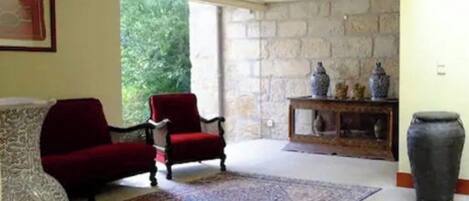 Una sala de estar con un sillón rojo, un tapete estampado, una pared de piedra y un jarrón grande.