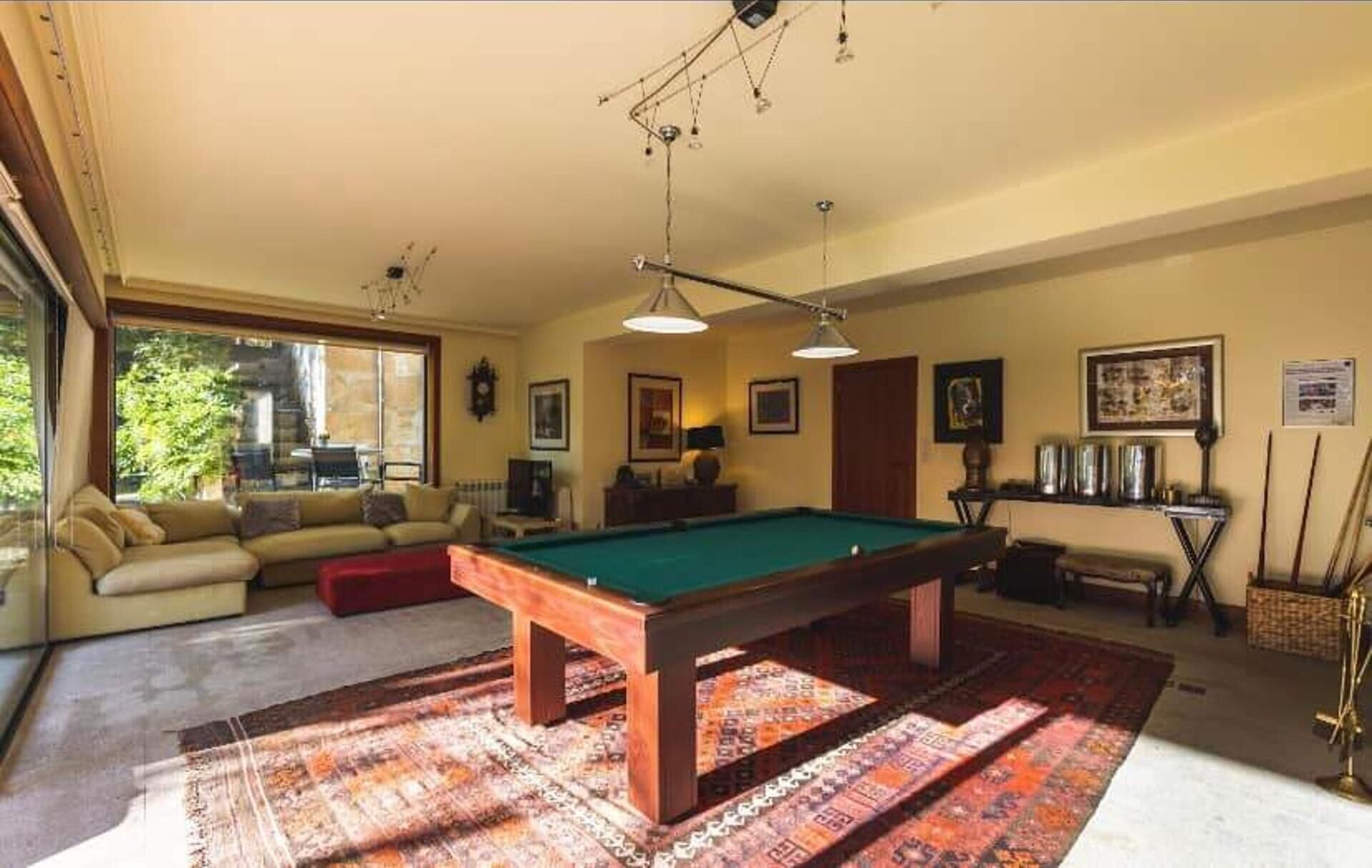A pool table in a room with a sofa, a lamp, and framed pictures on the wall.