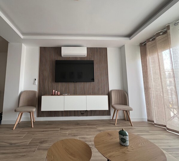 A modern living room with a flat-screen TV, two chairs, a coffee table, and a wooden floor.