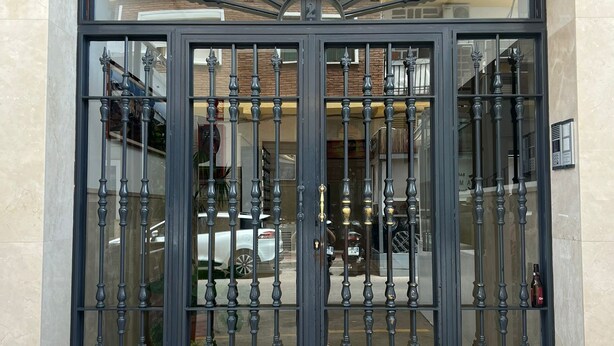 Un gran portón de metal ornamentado con el número '2' encima, que da acceso a un edificio con entrada de azulejos.