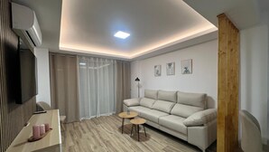 Una sala de estar moderna con sofá, mesa de centro, televisor y una lámpara de techo.