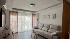 Una sala de estar con sofá, mesa de centro, televisor y un amplio ventanal con cortinas.