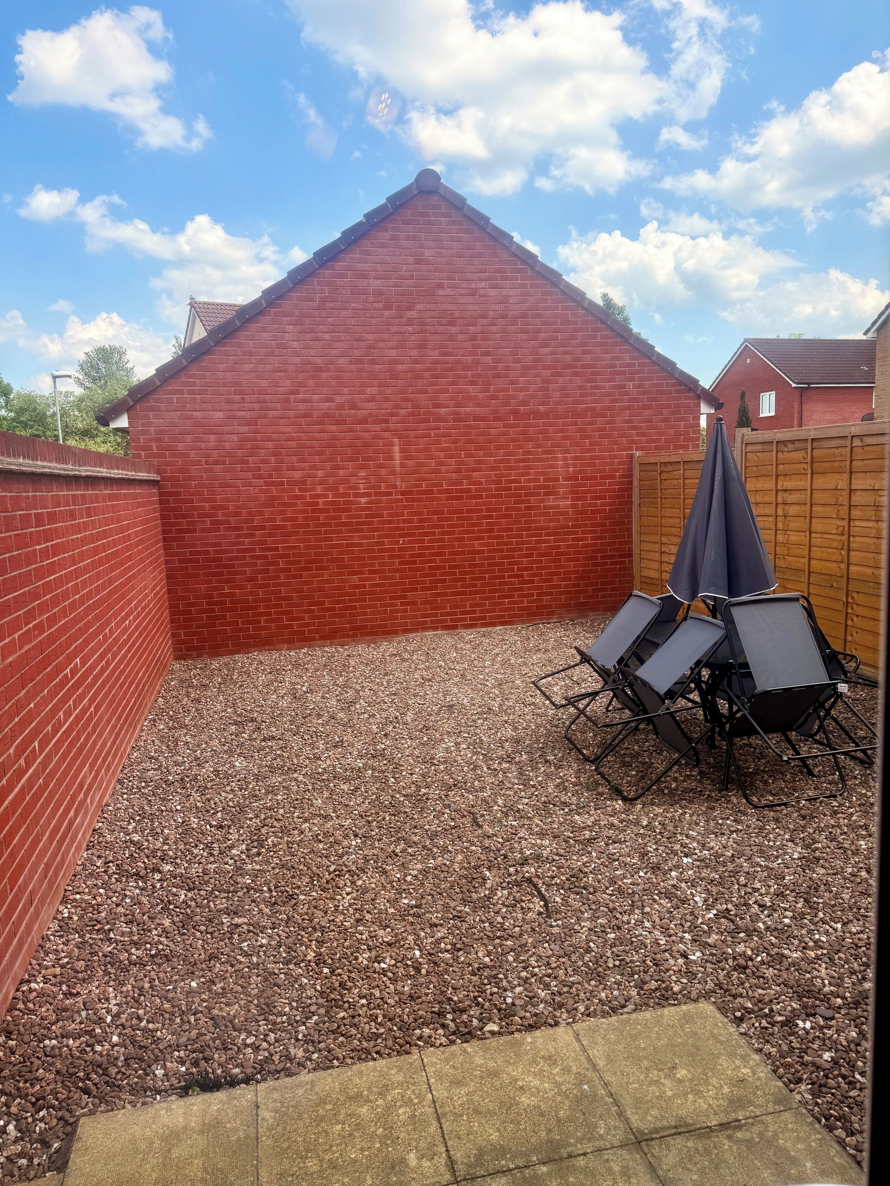 A backyard with a red brick wall, gravel ground, and a wooden fence.