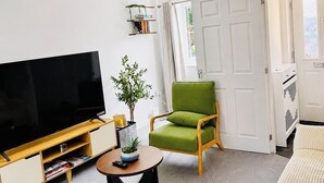Uma sala de estar com televisão de tela plana, poltronas verdes, uma mesa de centro e uma estante de livros.