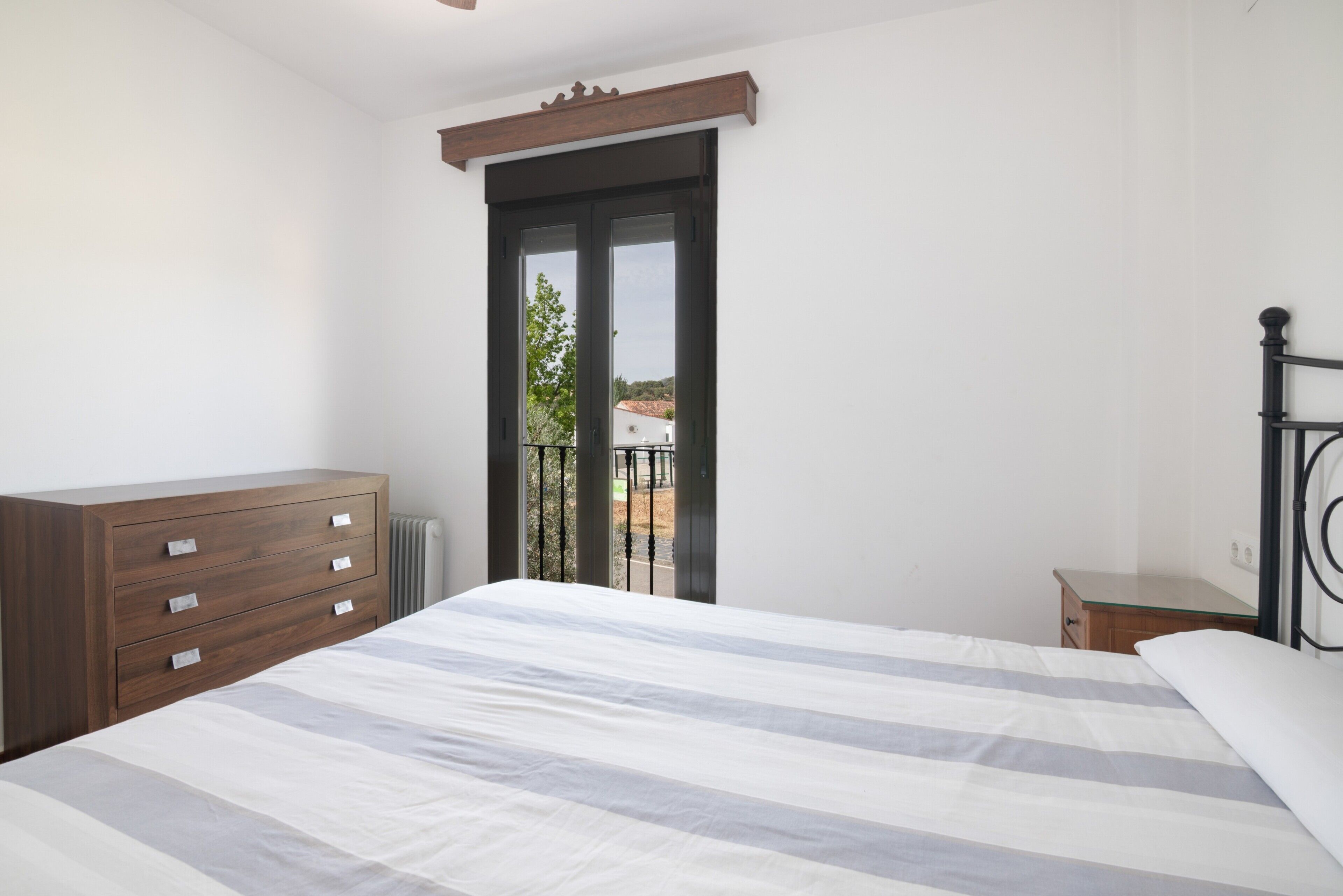 Un dormitorio con cama, cómoda, mesita de noche y puerta al balcón.