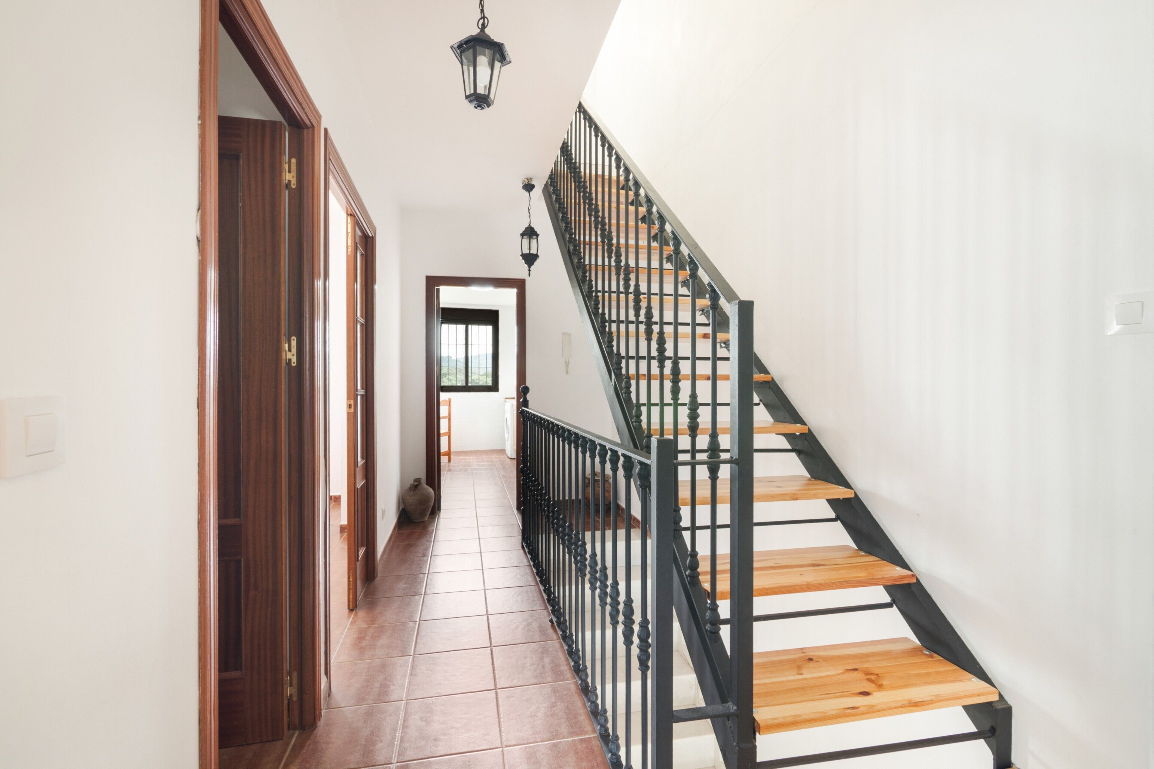 Un pasillo con una escalera de madera, una puerta y una lámpara colgante.