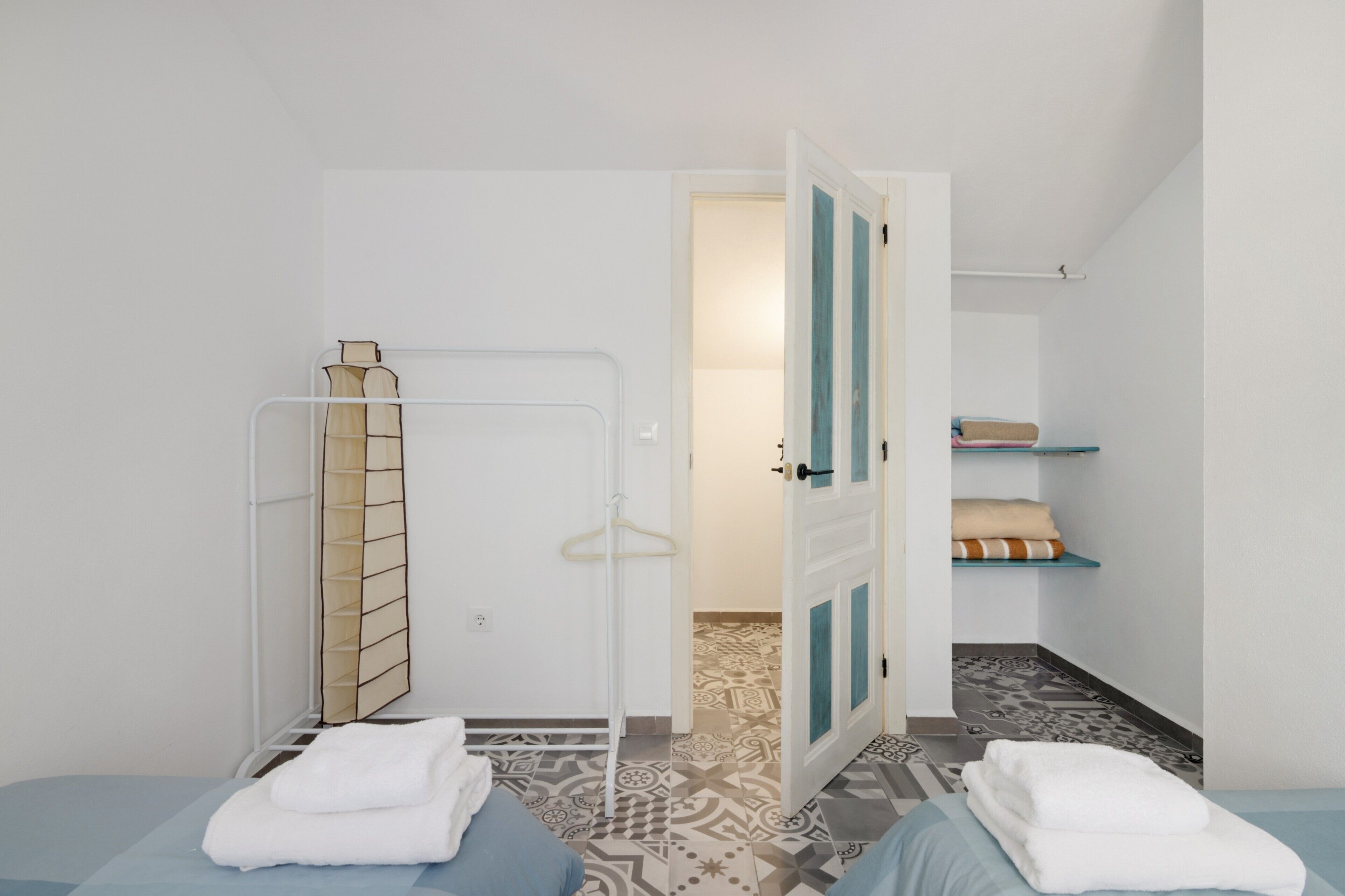 Una habitación con dos camas, un perchero, una puerta que da a otra habitación y suelo con estampado.