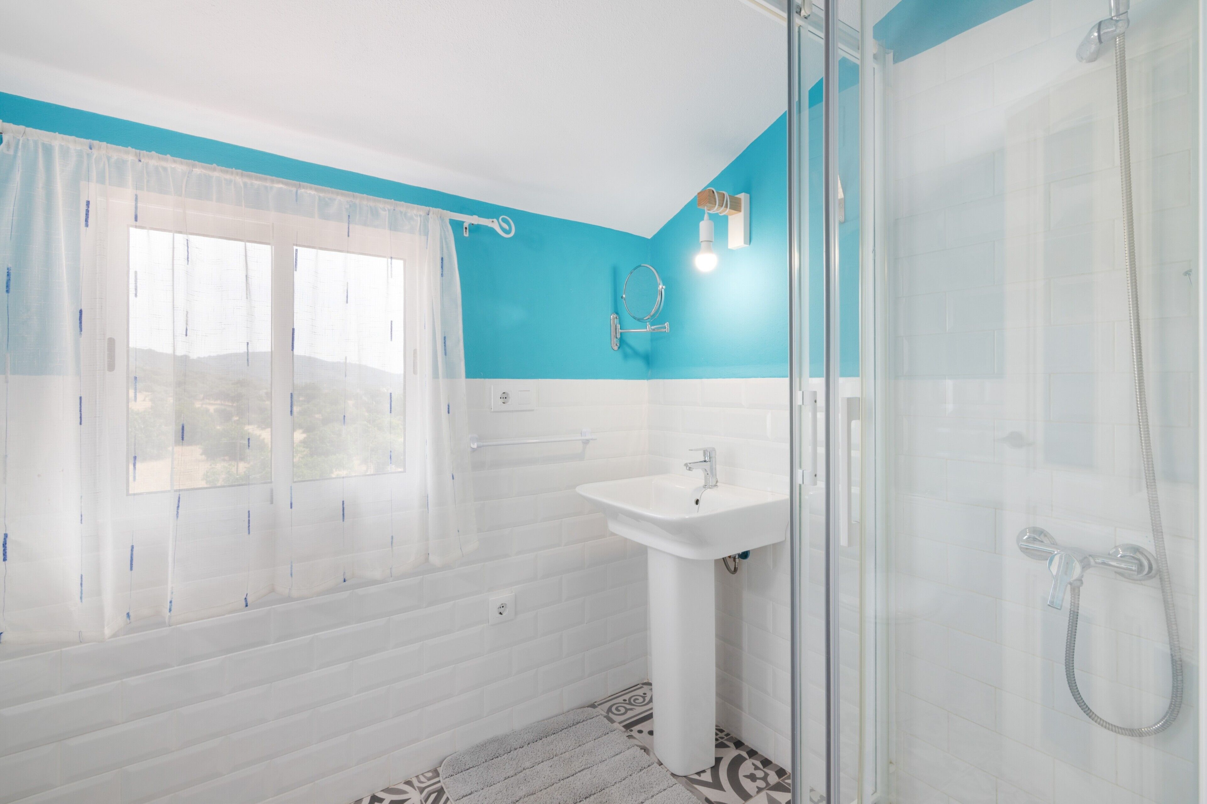 Un baño con ducha, lavamanos y ventana con cortinas.