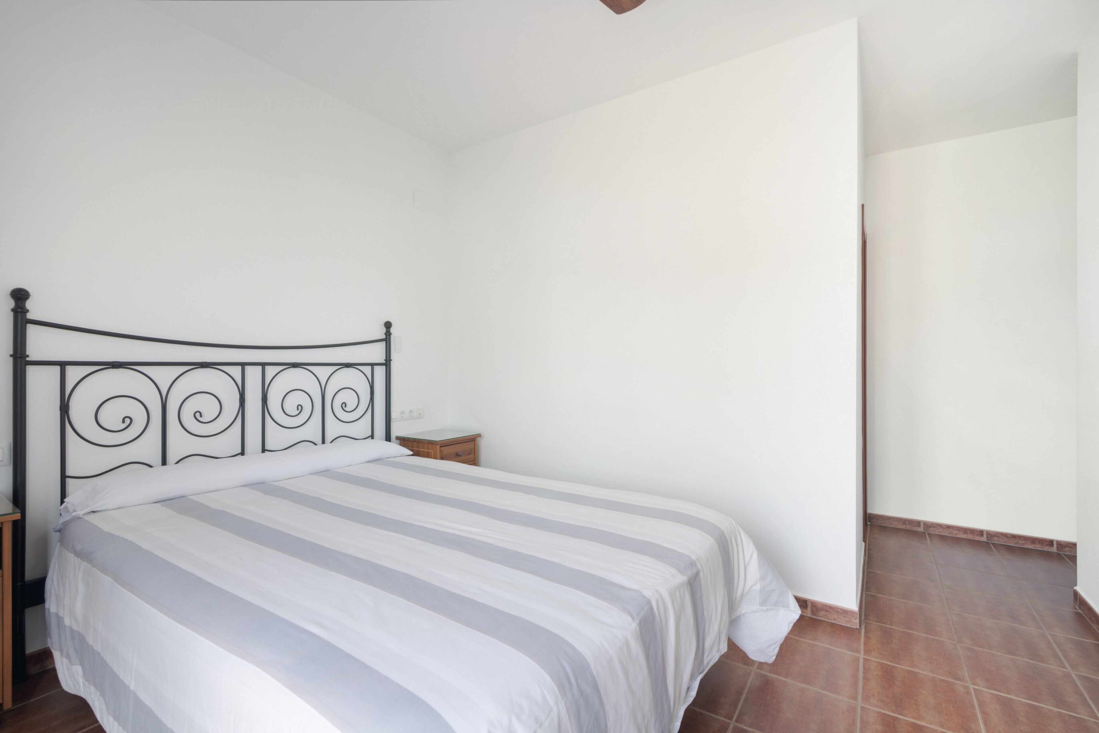 A bedroom with a bed, a nightstand, a wooden drawer, and a white wall.