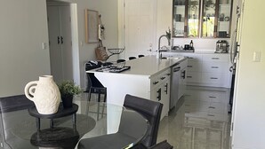 Una cocina moderna con una isla central, un comedor con mesa de vidrio y sillas de cuero negro.