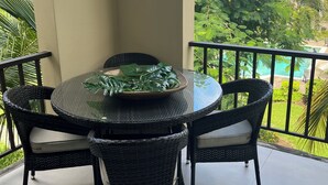 Una mesa redonda con sillas en un balcón, con vistas a una piscina y abundante vegetación.