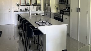 Una cocina moderna con una isla central, taburetes negros tipo barra, un microondas y un refrigerador.