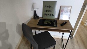 Een klein bureau met een stoel, een lamp, een motiverende poster en een afstandsbediening.