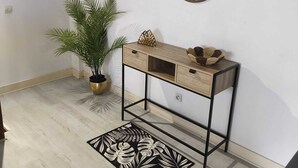 Een kamer met een houten console tafel, een potplant, een decoratief wandkunstwerk en een kamerbreed tapijt met dessin.