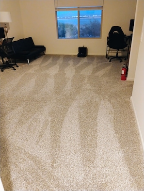 A carpeted room with a window, a black office chair, a black couch, and a fire extinguisher. -  4-bedroom in superb Tucson, Fully Furnished Escape Near Scenic Desert Trails (Tucson)