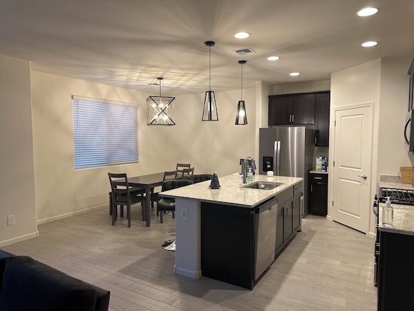 A modern kitchen with a central island, built-in appliances, pendant lighting, and a dining area with chairs. -  4-bedroom in superb Tucson, Fully Furnished Escape Near Scenic Desert Trails (Tucson)