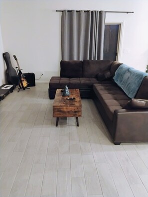 A living room with a brown sofa, a wooden coffee table, a guitar, and a speaker. -  4-bedroom in superb Tucson, Fully Furnished Escape Near Scenic Desert Trails (Tucson)