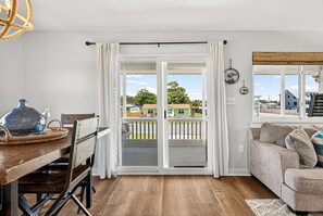 Ein Zimmer mit einem Holzesstisch, Stühlen, einer Couch, einem Balkon mit Geländer und Blick auf Häuser.