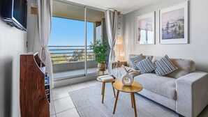 A modern living room with a sofa, a coffee table, a TV, and a balcony with a view. - Relaxing Family Condo with Ocean View & Pools in Costa Algarrobo (El Yeco)