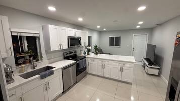 A modern kitchen with white cabinets, stainless steel appliances, and a tiled floor.
