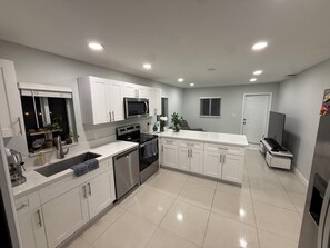 A modern kitchen with white cabinets, stainless steel appliances, and a tiled floor. - 1-bedroom house w/ pool in quaint Margate FL 20 min to Pompano beach attractions (Margate)