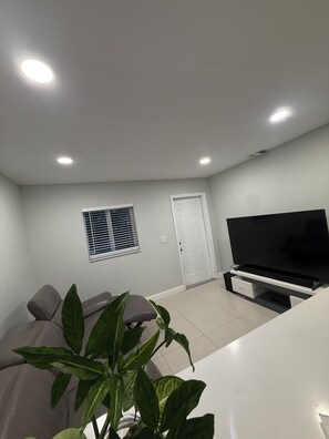 A living room with a sofa, a TV, a window with blinds, and a door. - 1-bedroom house w/ pool in quaint Margate FL 20 min to Pompano beach attractions (Margate)