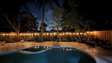A backyard with a swimming pool, wooden fence, and potted plants.
