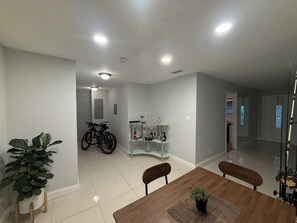 A dining area with a wooden table, chairs, a potted plant, a glass cabinet with bottles, and bicycles in the background. - 1-bedroom house w/ pool in quaint Margate FL 20 min to Pompano beach attractions (Margate)