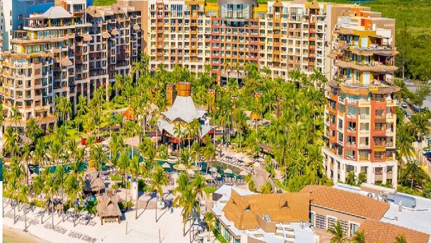 A resort with multiple high-rise buildings, a beach area with umbrellas, and palm trees.