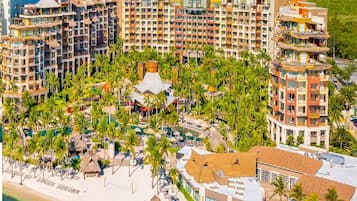 Un resort con varios edificios de gran altura, una zona de playa con sombrillas y palmeras.