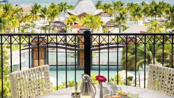 Un balcón con mesa lista para el desayuno con vista a un complejo turístico con piscina y palmeras.