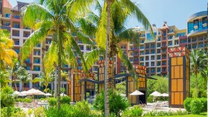 A resort with multiple-story buildings, palm trees, and a pool area with umbrellas.