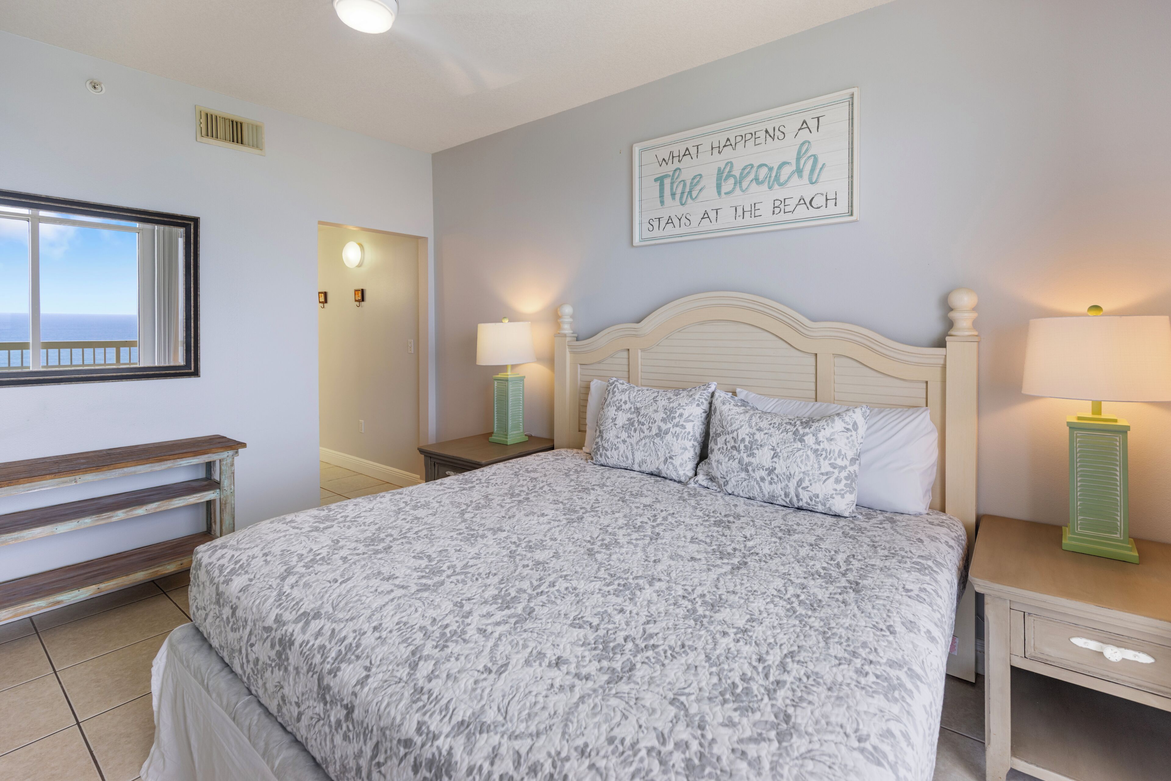 A bedroom with a bed, two bedside tables, a nightstand, a window with a view, and a wall sign.